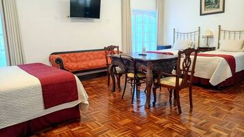 Habitación de hotel con dos camas, una mesa de comedor con sillas, un televisor y un cuadro en la pared.