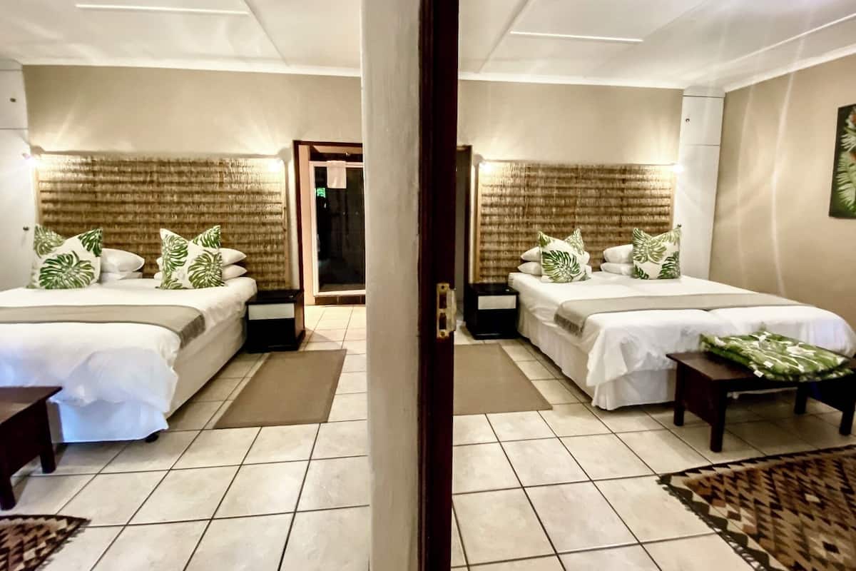 A hotel room with two beds, a door, and a view of the outside.