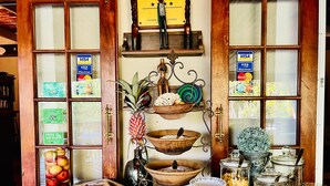 A breakfast buffet with various food items and utensils, a wooden display shelf with decorative items, and a window with Visa and Mastercard logos. - Lidiko Lodge (St. Lucia)