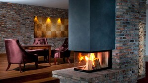 A room with a brick fireplace, wooden steps, and a dining area with chairs. - Hotel Remes (Opalenica)