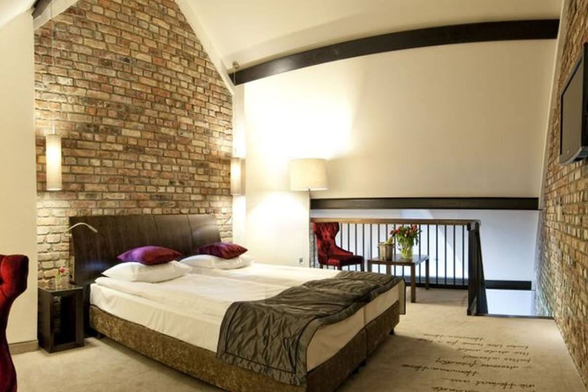 Un dormitorio con chimenea de ladrillo, una cama con almohadas, una silla roja y un balcón con barandilla.