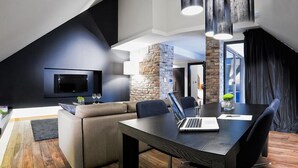A modern interior with a dark-colored sofa, a wooden dining table with a laptop, and a stone accent wall. - Hotel Remes (Opalenica)