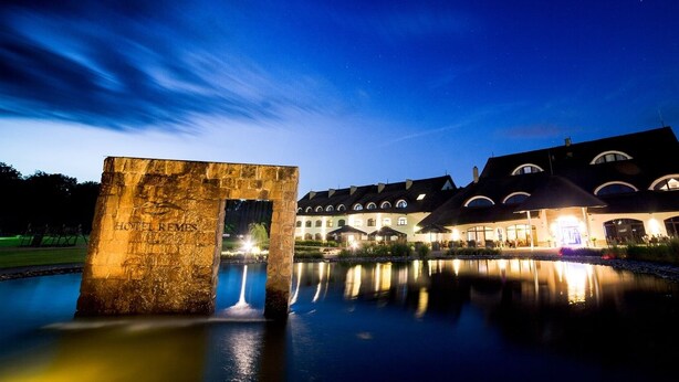 A stone structure with "HOTEL REMES" engraved, a reflective pool, and a building with multiple arched windows and a roof with dormer windows. - Hotel Remes (Opalenica)