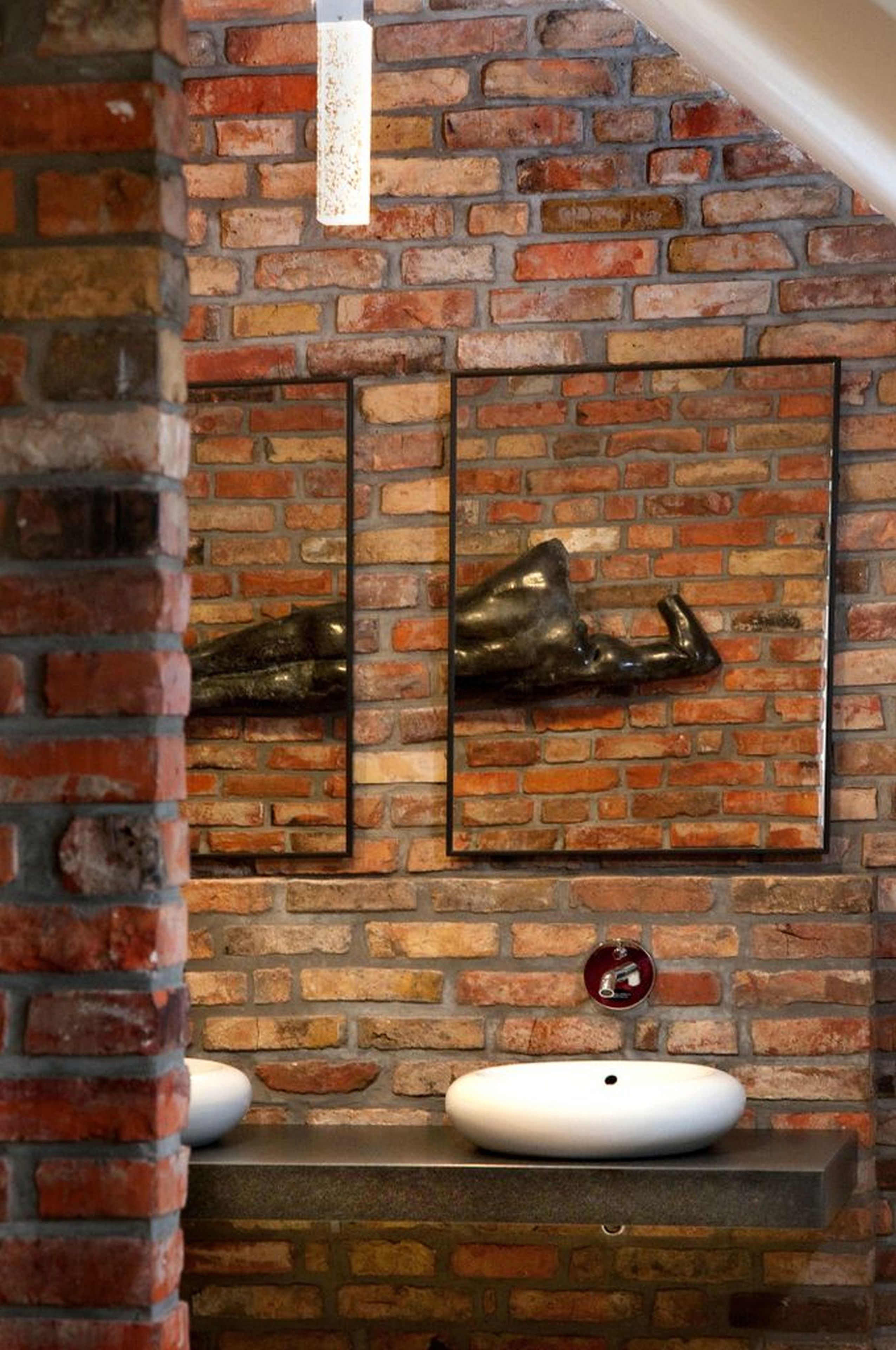 A brick wall with two framed animal sculptures and a white sink.