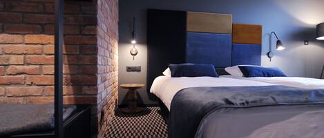 Une chambre d’hôtel moderne avec un mur en briques, un sol à carreaux, un lit avec une literie bleue et des luminaires fixés au mur.