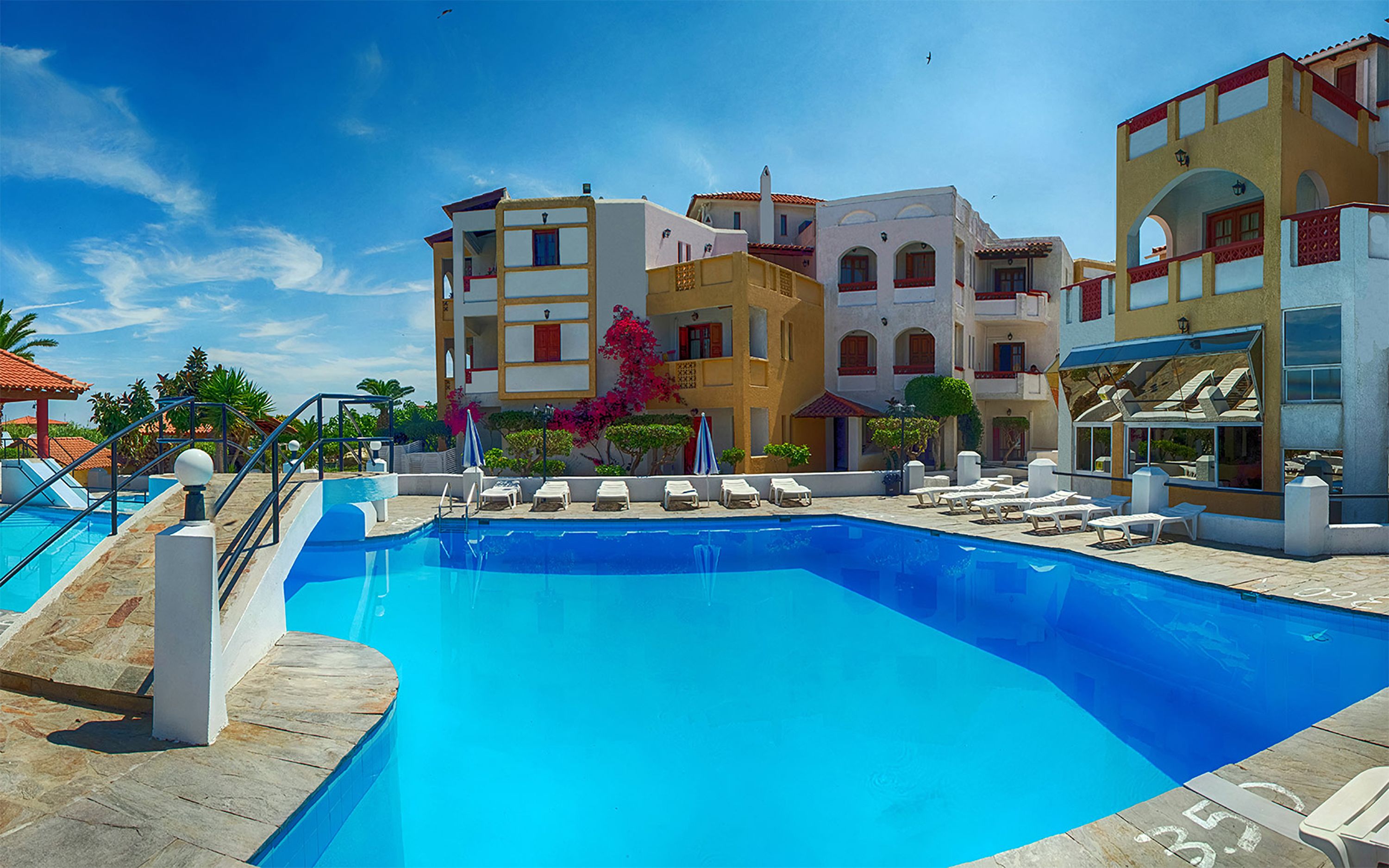 A hotel with a swimming pool, multiple balconies, and a clear blue sky.