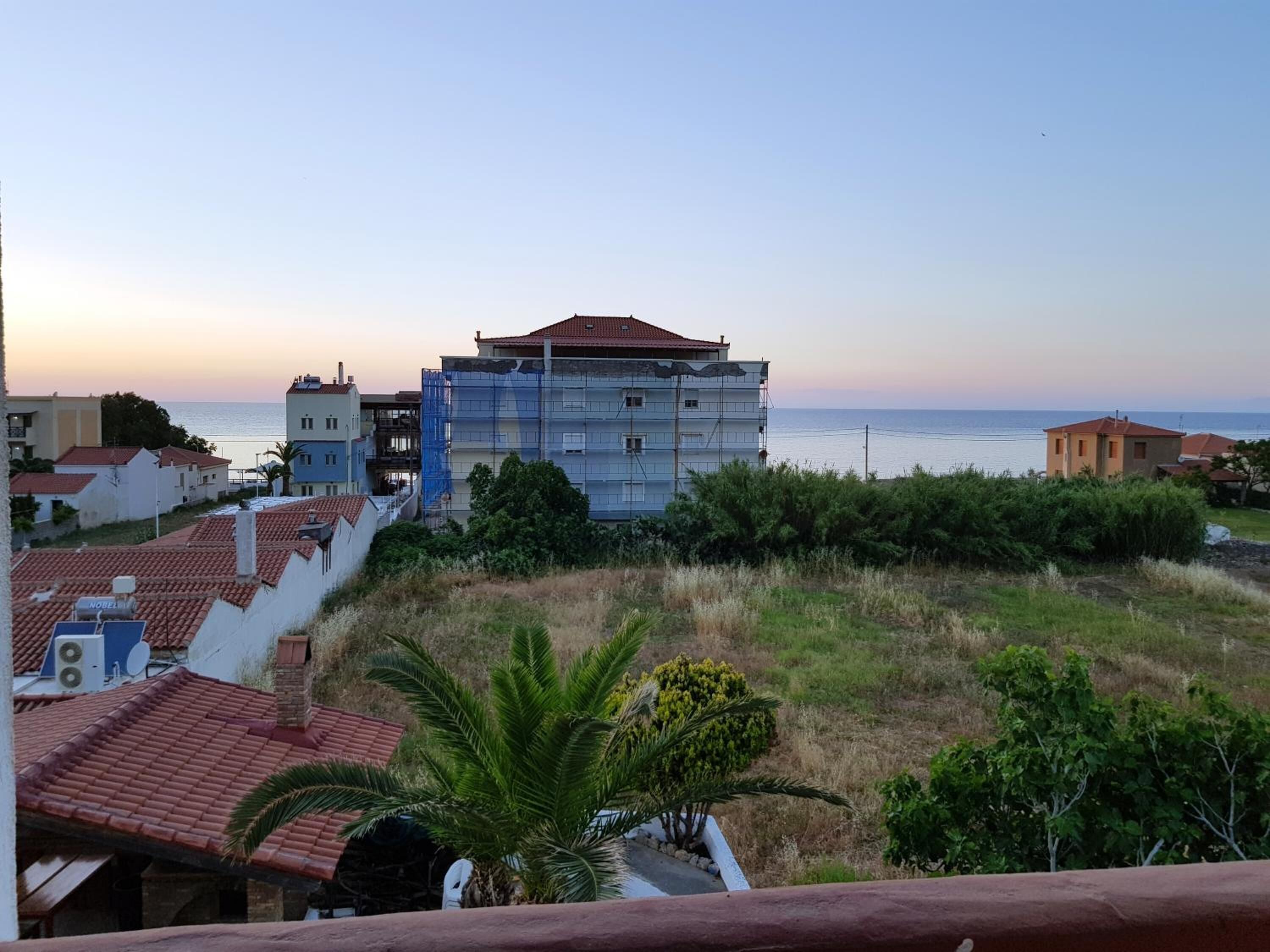 A coastal building with a red-tiled roof, surrounded by greenery and a view of the sea.