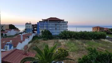 A coastal building with a red-tiled roof, surrounded by greenery and a view of the sea.