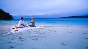 Twee personen zitten op het strand met een deken, omringd door kaarsen.