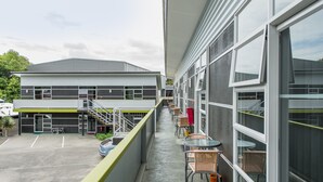 A building with a covered outdoor area featuring a row of tables and chairs, a staircase, and a parking lot. - 151 on London Motel (Whanganui)