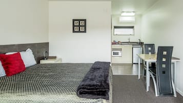 Quarto de hotel com cama, escrivaninha e cozinha compacta.