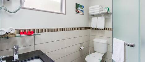 A bathroom with a sink, toilet, and a window. There are towels and toiletries on shelves.