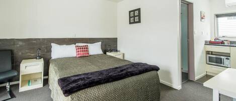 A hotel room with a bed, bedside tables, a small desk, a microwave, and a door leading to another room.