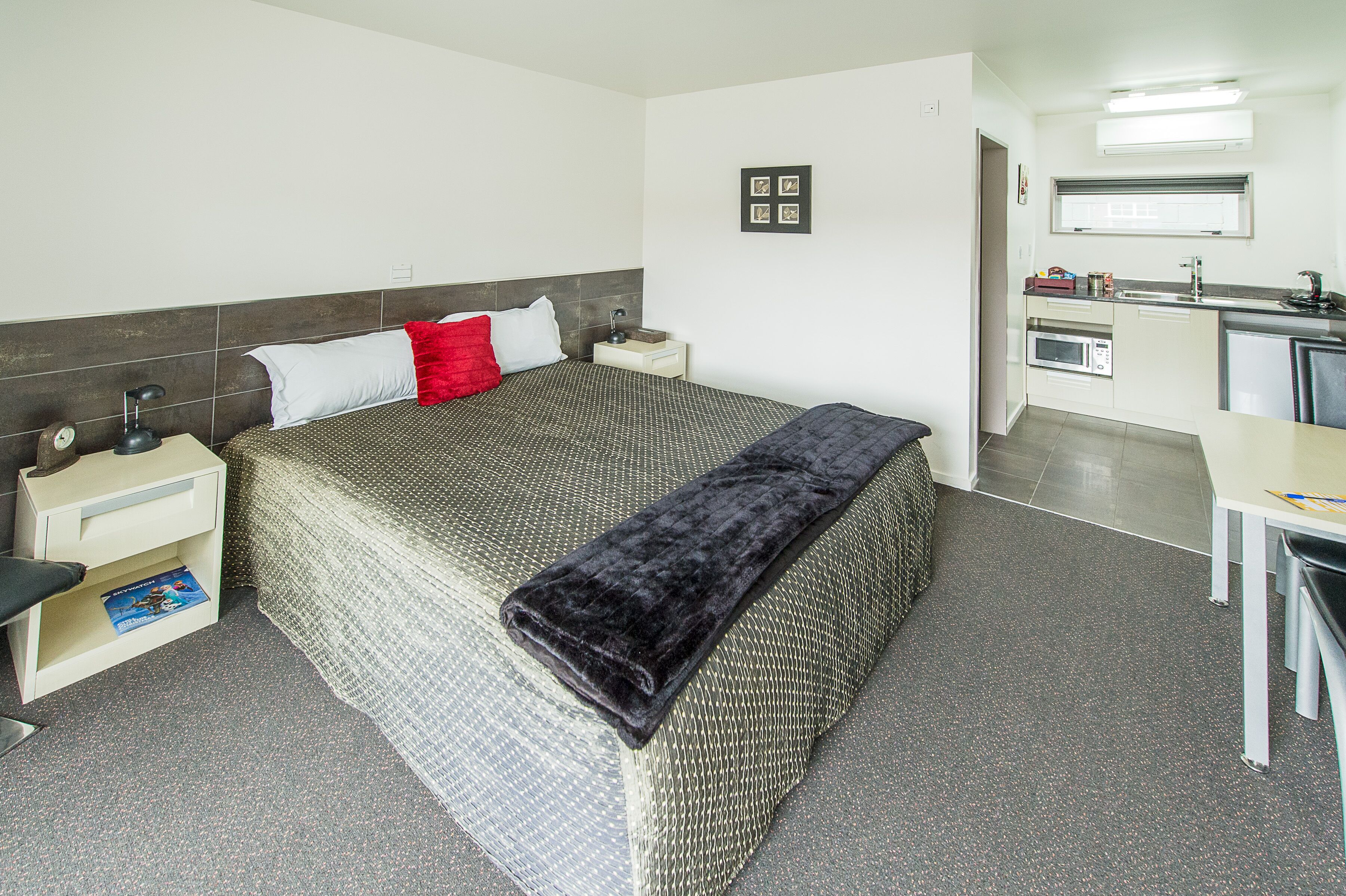 A hotel room with a bed, bedside tables, a desk, a kitchenette, and a bathroom.