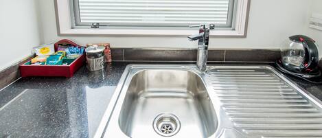 A stainless steel kitchen sink with a window above it, a red dish rack, and a kettle on the counter.
