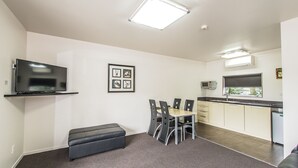 A modern kitchen with a flat-screen TV, a dining area with a bench, and a framed picture on the wall. - 151 on London Motel (Whanganui)
