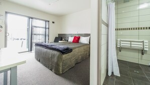 A hotel room with a bed, a desk, a shower area, and a view of the outside. - 151 on London Motel (Whanganui)