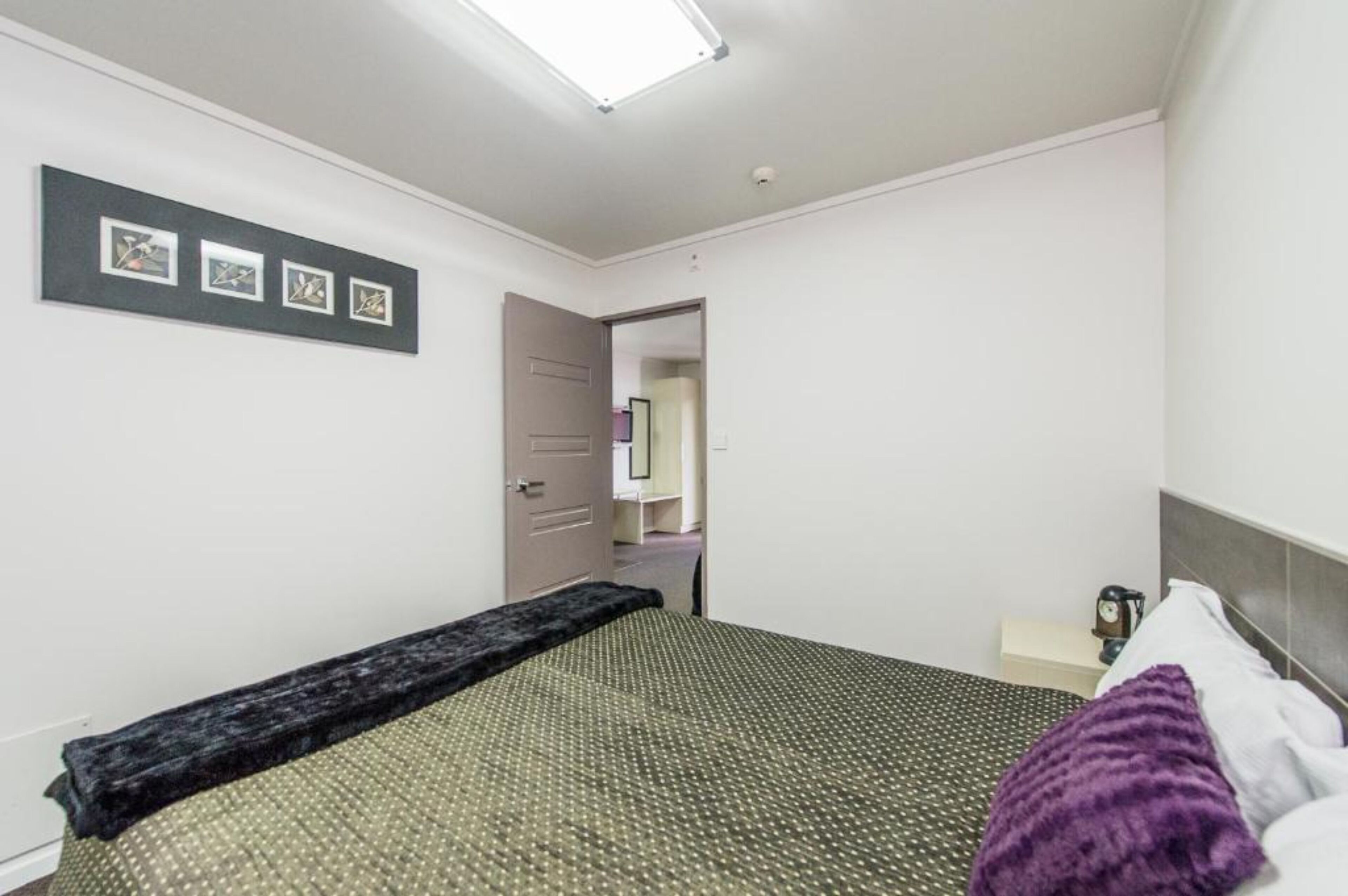 Un dormitorio con cama, mesita de noche, lámpara y una puerta que da a otra habitación.