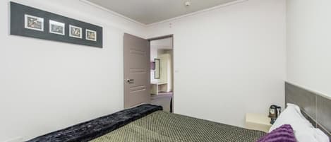 Un dormitorio con cama, mesita de noche, lámpara y una puerta que da a otra habitación.
