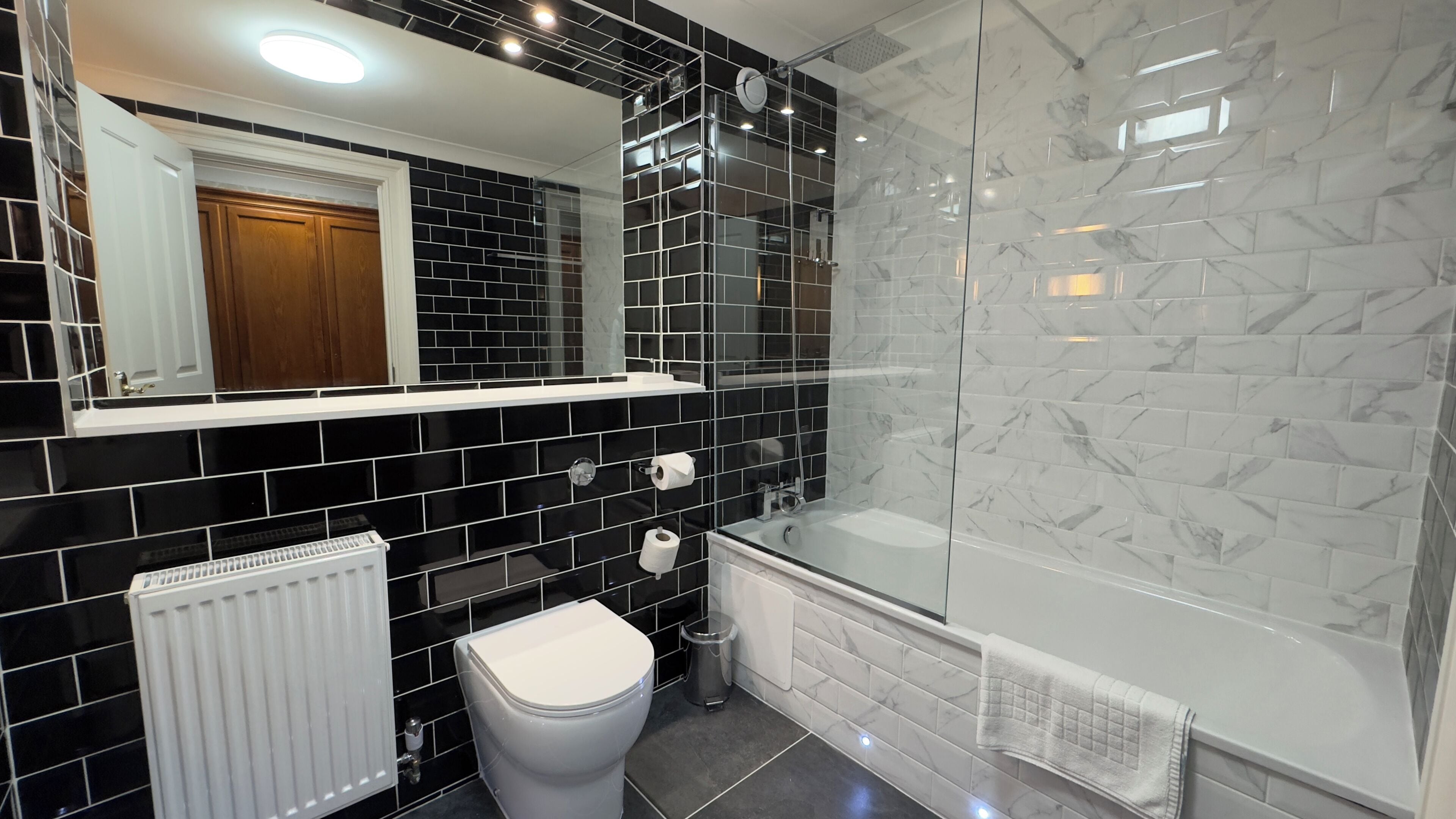 A modern bathroom with black and white tiled walls, a white toilet, a white sink, and a glass-enclosed shower.