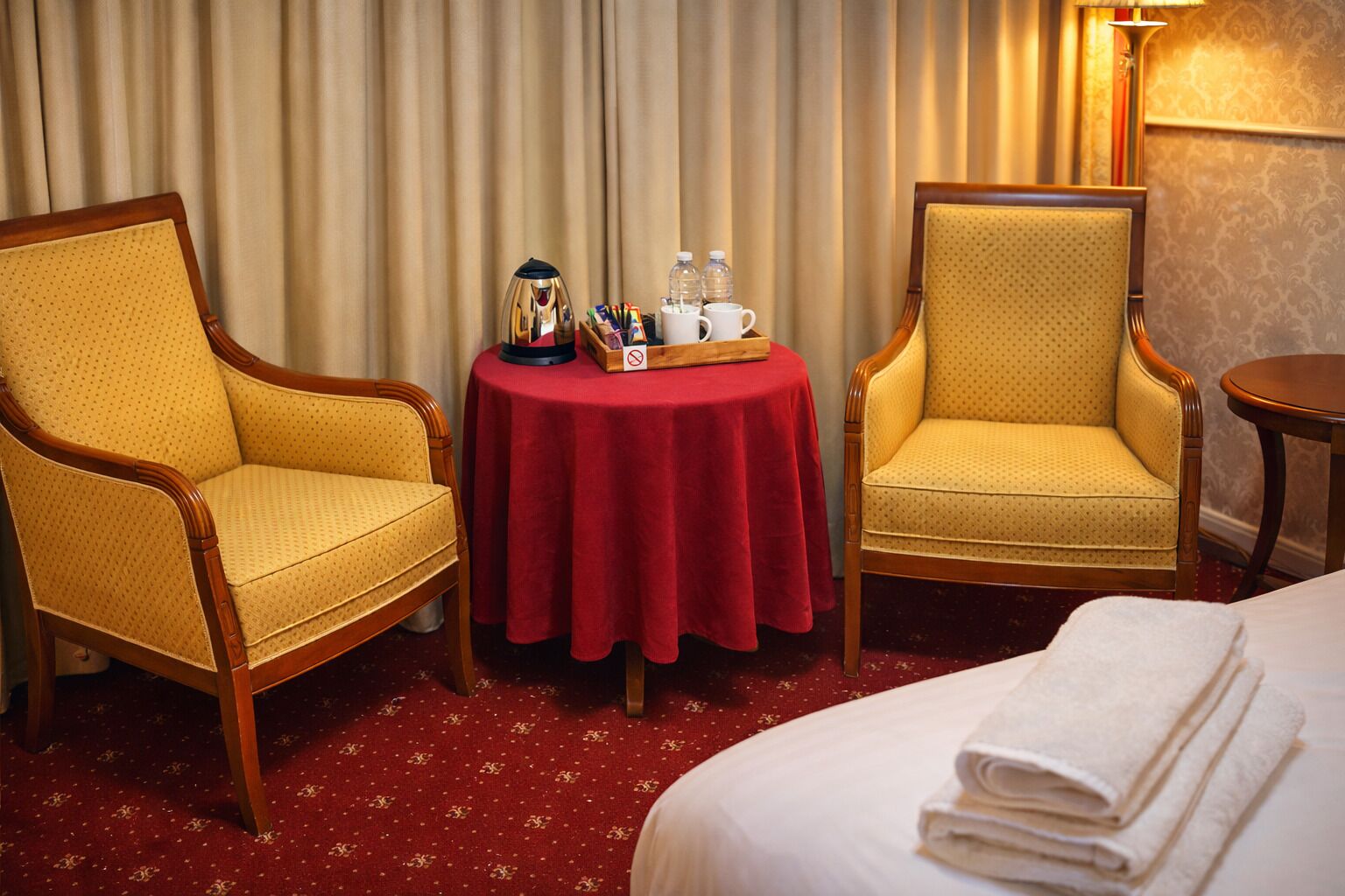 A hotel room with two armchairs, a small round table with amenities, and a neatly made bed.