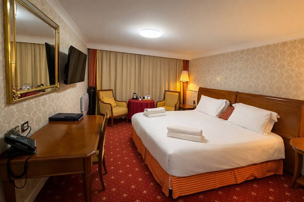 Een hotelkamer met een groot bed, een bureau met telefoon, een stoel, een tafel met lamp en een televisie aan de muur.