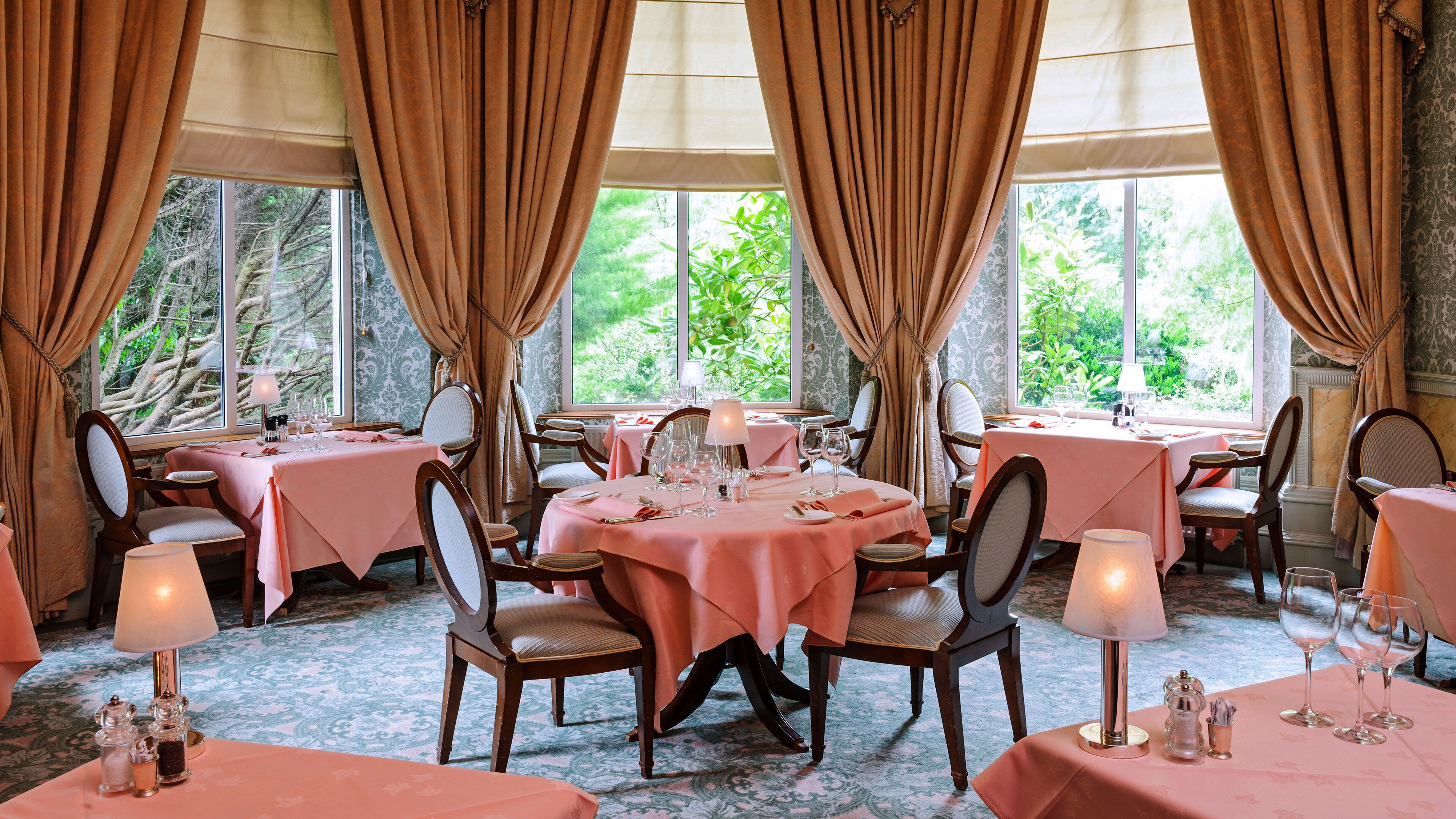 A dining area with tables set for four, each with a pink tablecloth and chairs.