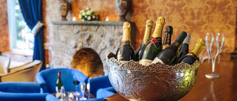 A room with a fireplace, a blue armchair, and a large bowl filled with champagne bottles.