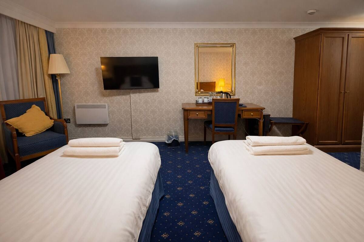 Een hotelkamer met twee bedden, een bureau, een stoel, een televisie, een spiegel en een kledingkast.