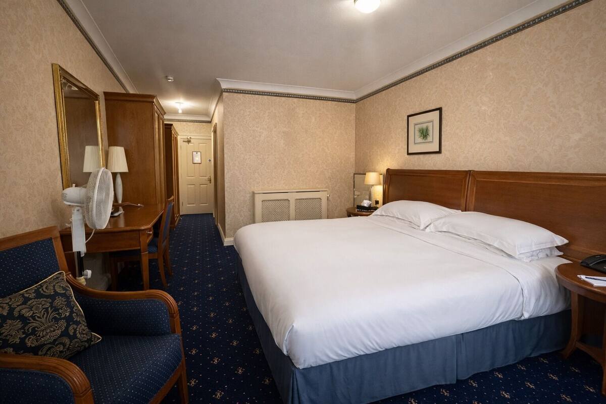 Een hotelkamer met een groot bed, een stoel, een bureau met lamp en een spiegel.