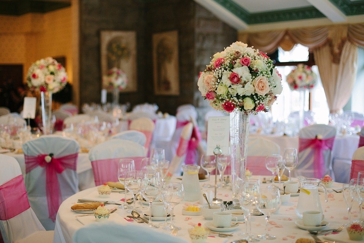 A banquet hall with round tables set for a formal event, adorned with floral centerpieces and white tablecloths.