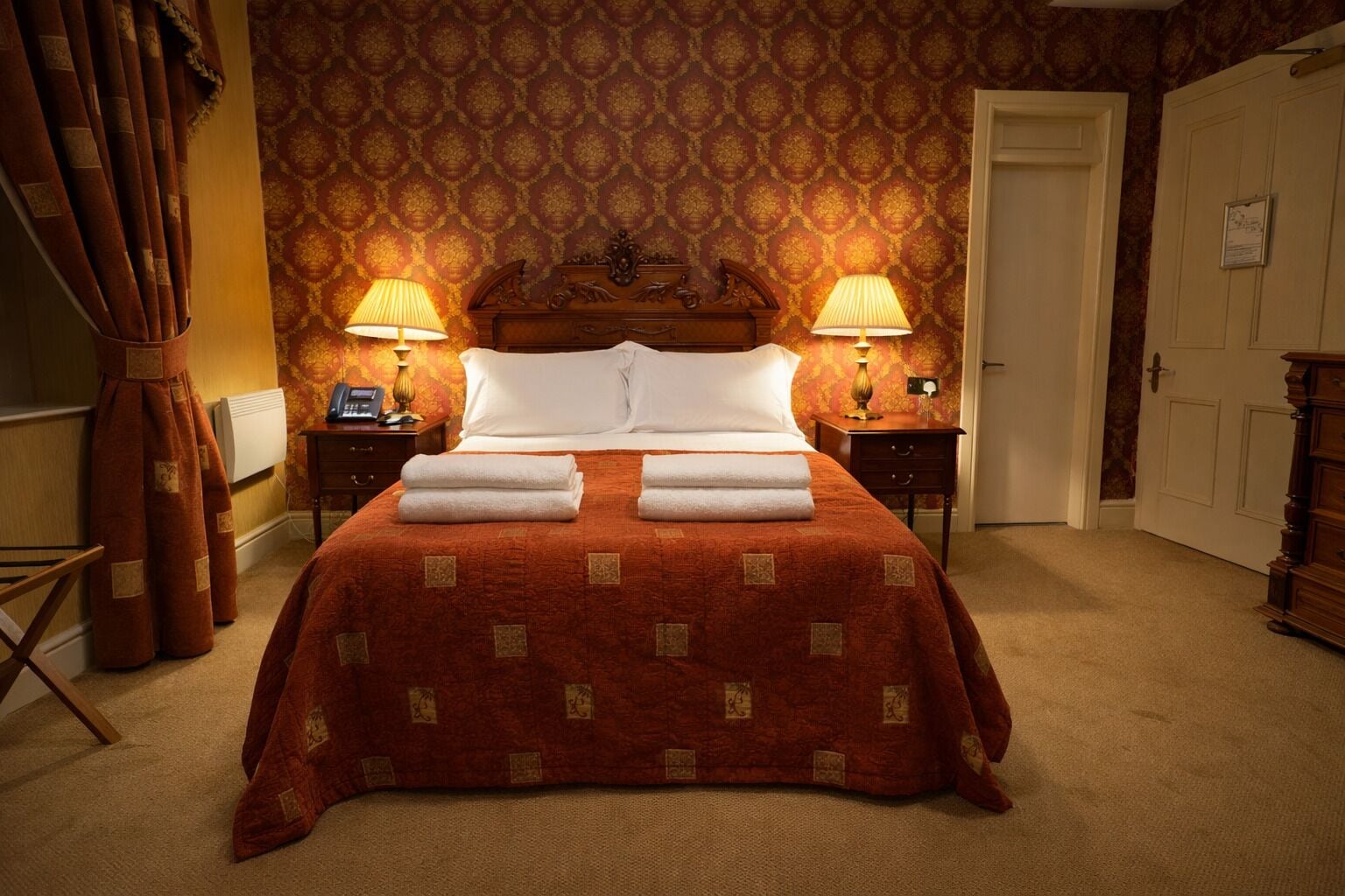 A neatly made bed with a red bedspread and white pillows, two bedside lamps, and a wooden headboard.