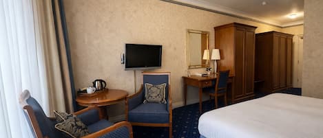Habitación de hotel con cama, dos sillones, un escritorio con silla, televisión, armario y una mesita con tetera.