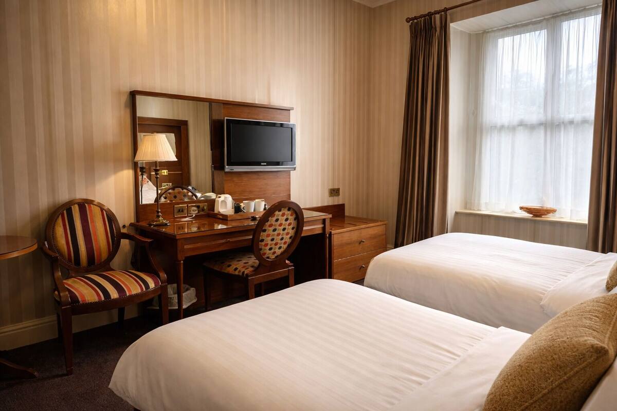 Een hotelkamer met twee bedden, een bureau met een televisie, een stoel en een raam met gordijnen.