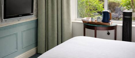 A hotel room with a bed, a television, a coffee maker, and a window with a view of greenery.