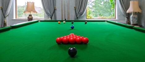 Une table de billard avec les billes disposées en forme de triangle, une fenêtre avec des rideaux et une lampe à l’arrière-plan.