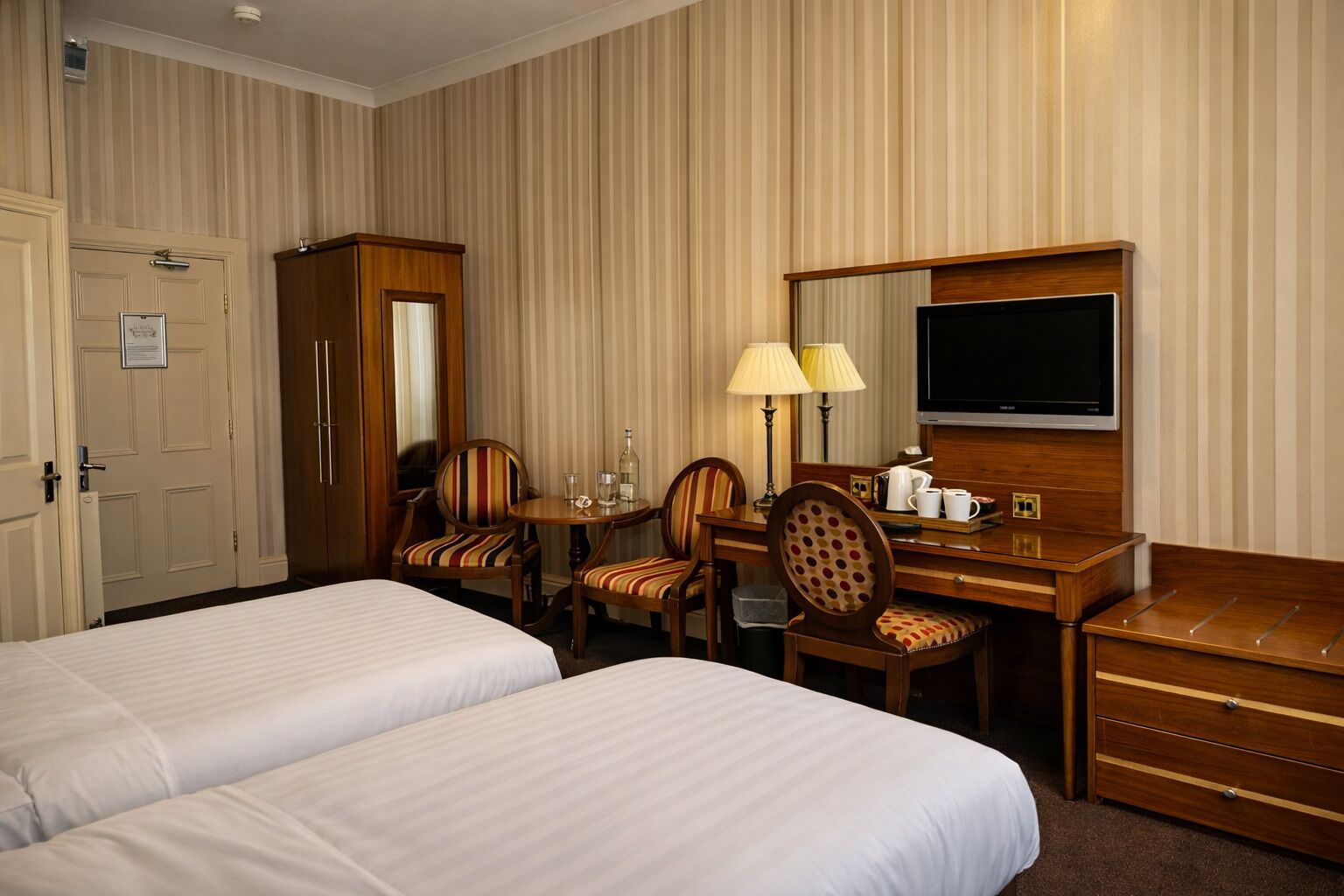 Ein Hotelzimmer mit zwei Betten, einem Schreibtisch mit Stuhl, einem Fernseher und einem Kleiderschrank.