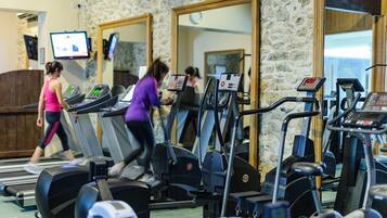 Un gimnasio con cintas de correr, bicicletas estáticas y un espejo grande.