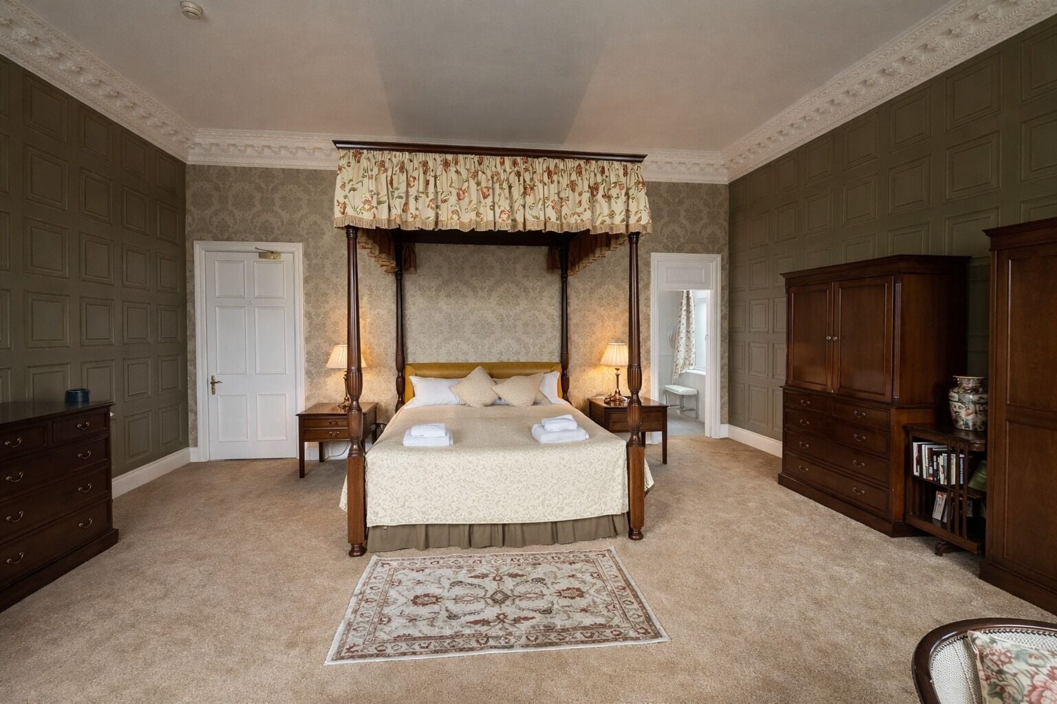 A four-poster bed with a canopy, a wooden wardrobe, a nightstand with a lamp, and a carpeted floor.
