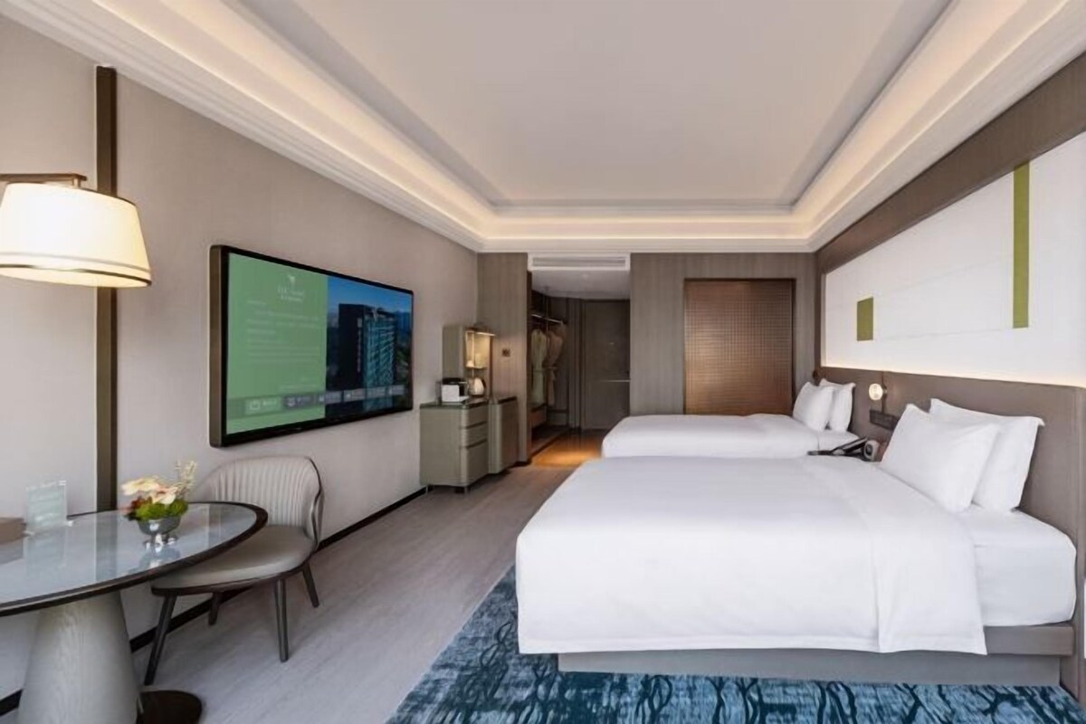 A hotel room with a large bed, a desk with a chair, a television, and a bathroom visible through an open door.