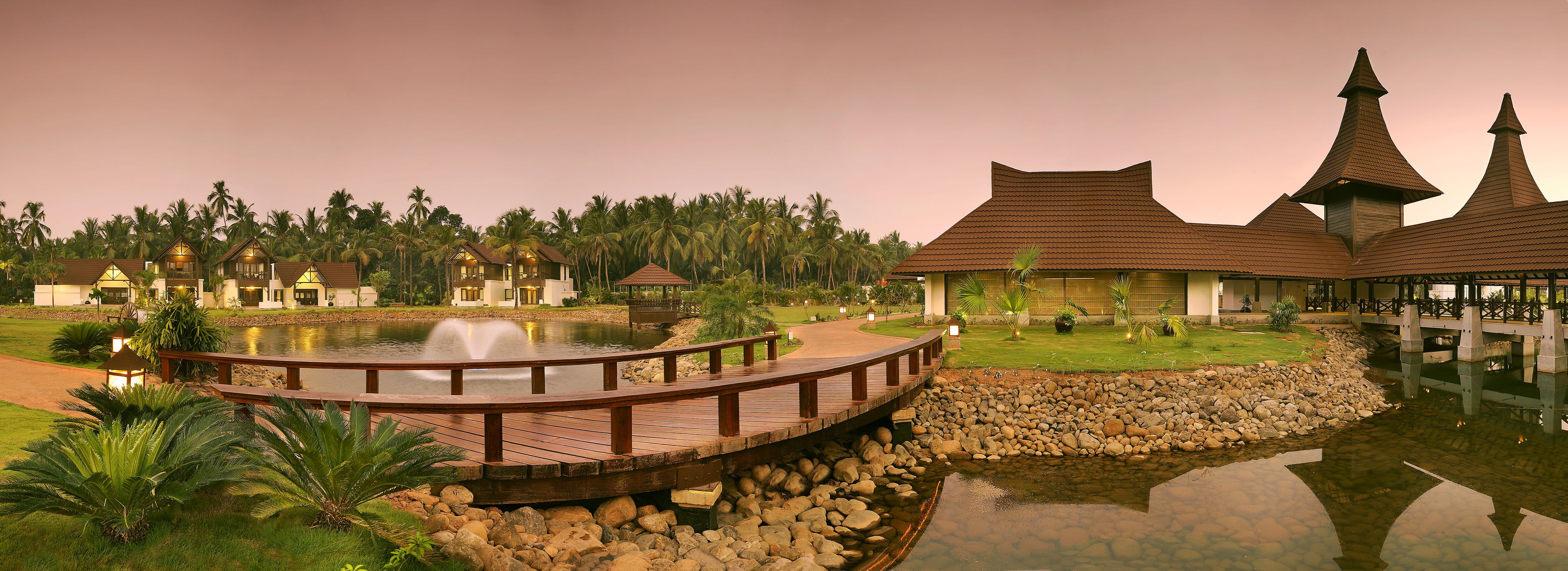 A resort with multiple bungalow-style buildings, a wooden bridge over a pond, and a well-maintained lawn area.