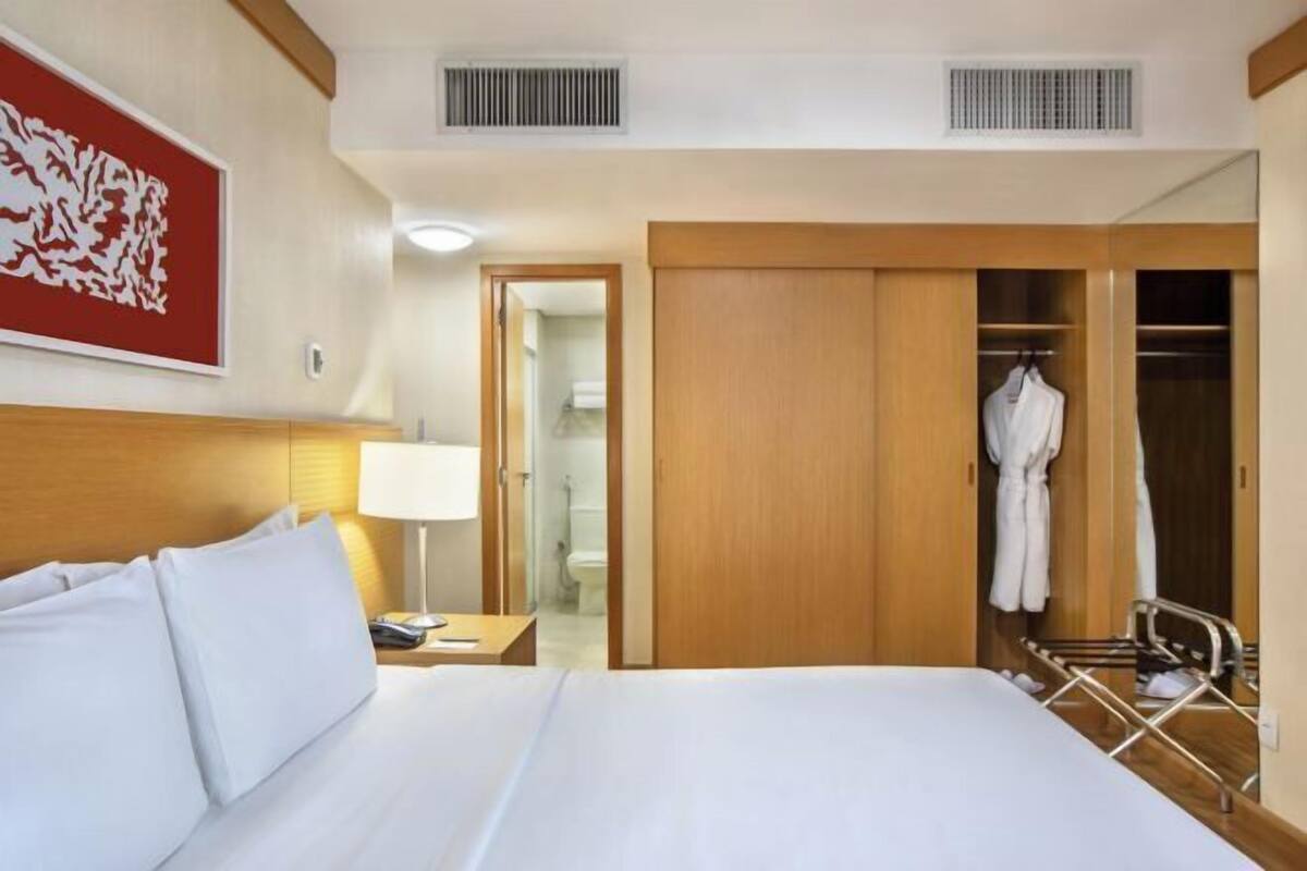 Une chambre d’hôtel comprenant un lit, une table de chevet, une lampe, une armoire et un miroir.