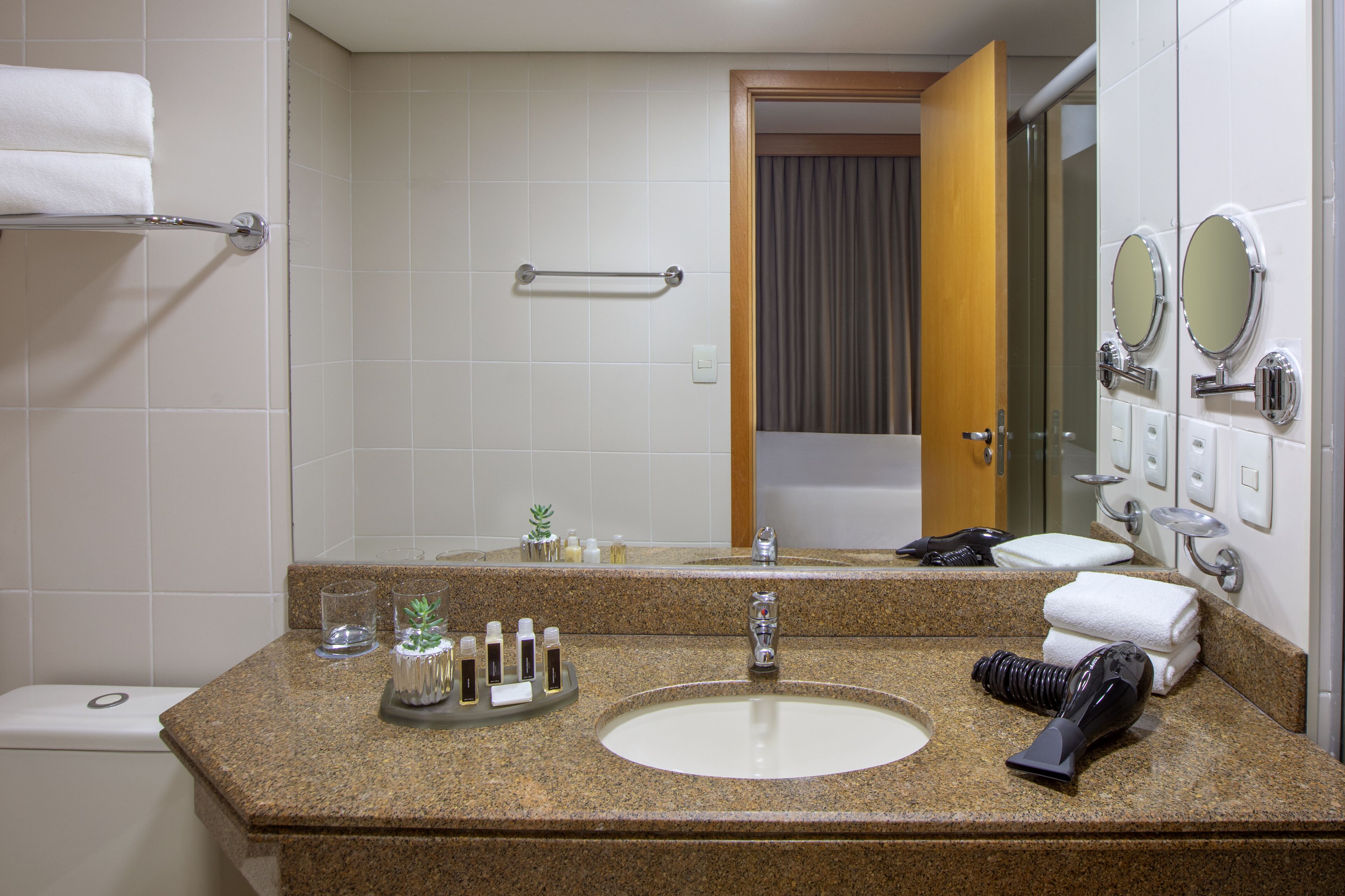 A bathroom with a granite countertop, a sink, a mirror, a towel rack, and a shower area.