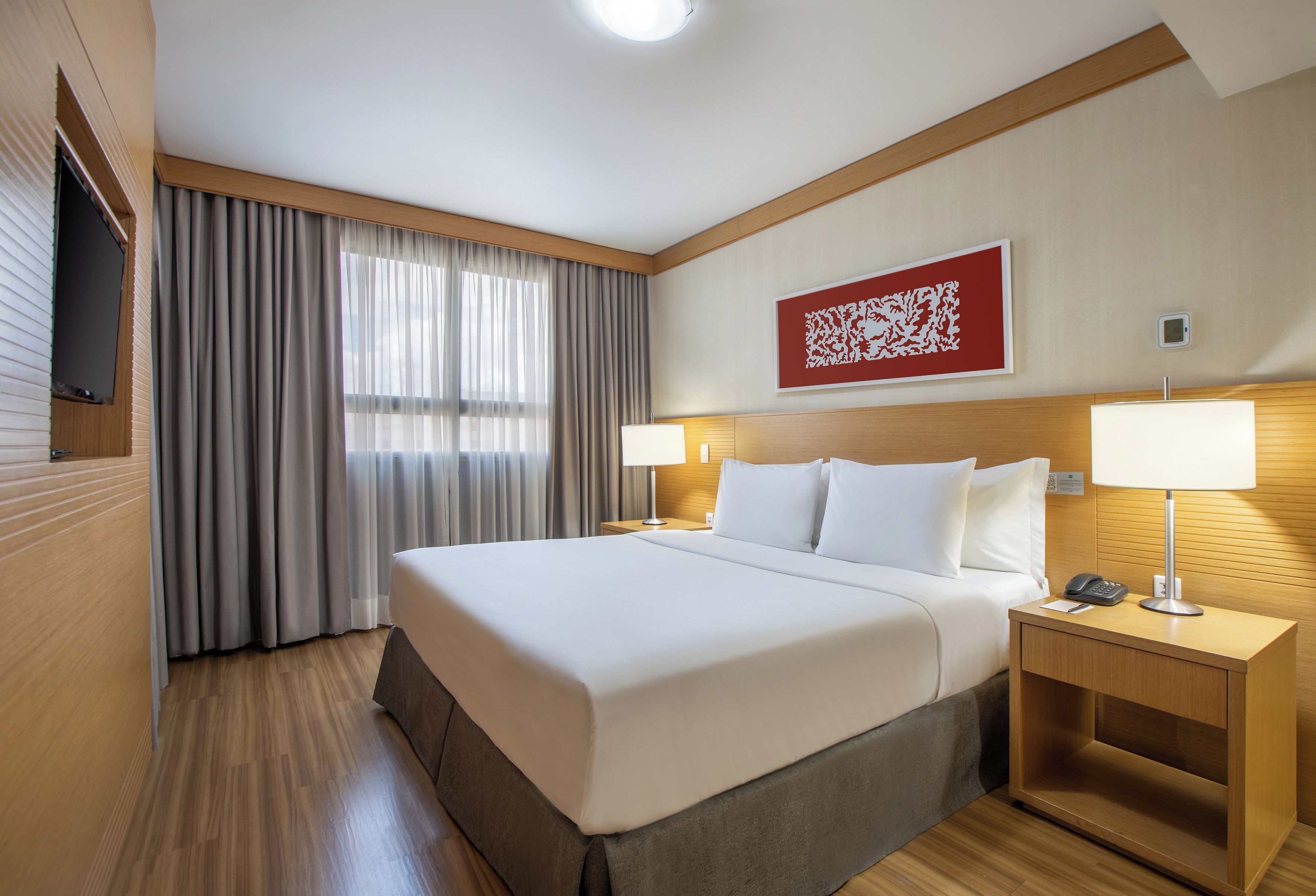 Een hotelkamer met een groot bed, twee bedlampen, een flatscreen televisie en een abstract kunstwerk in rood op de muur.
