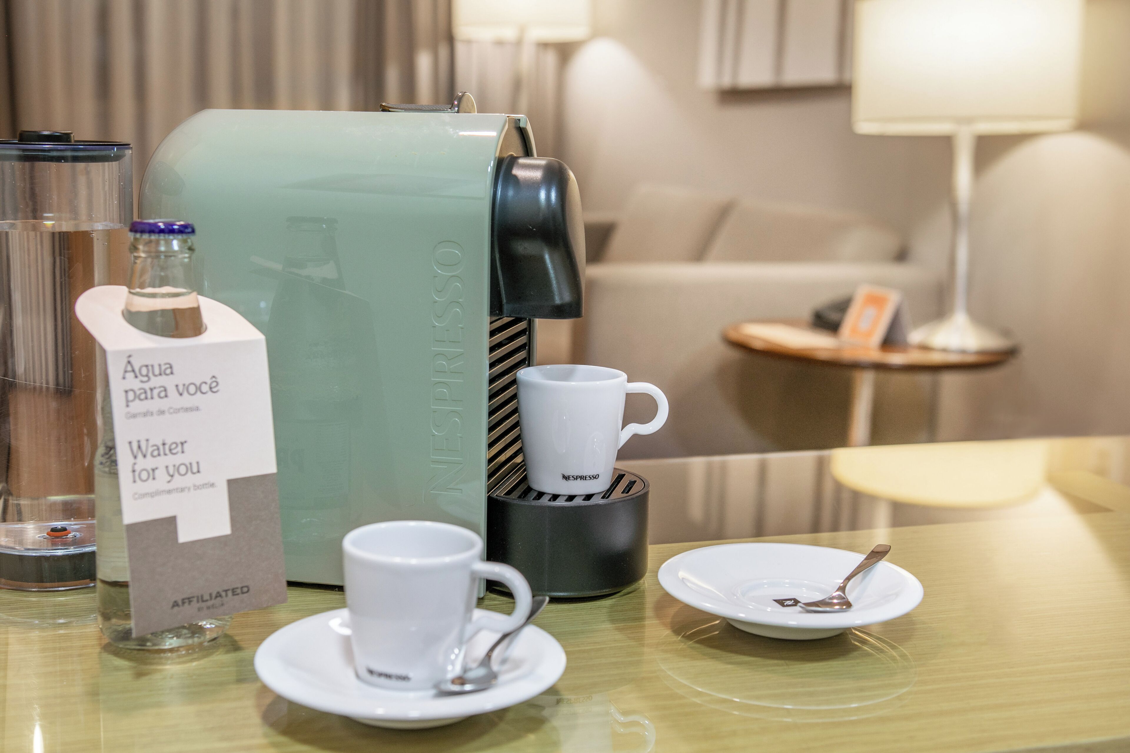 Habitación de hotel con una máquina de café Nespresso, una botella de agua y una taza sobre la mesa.