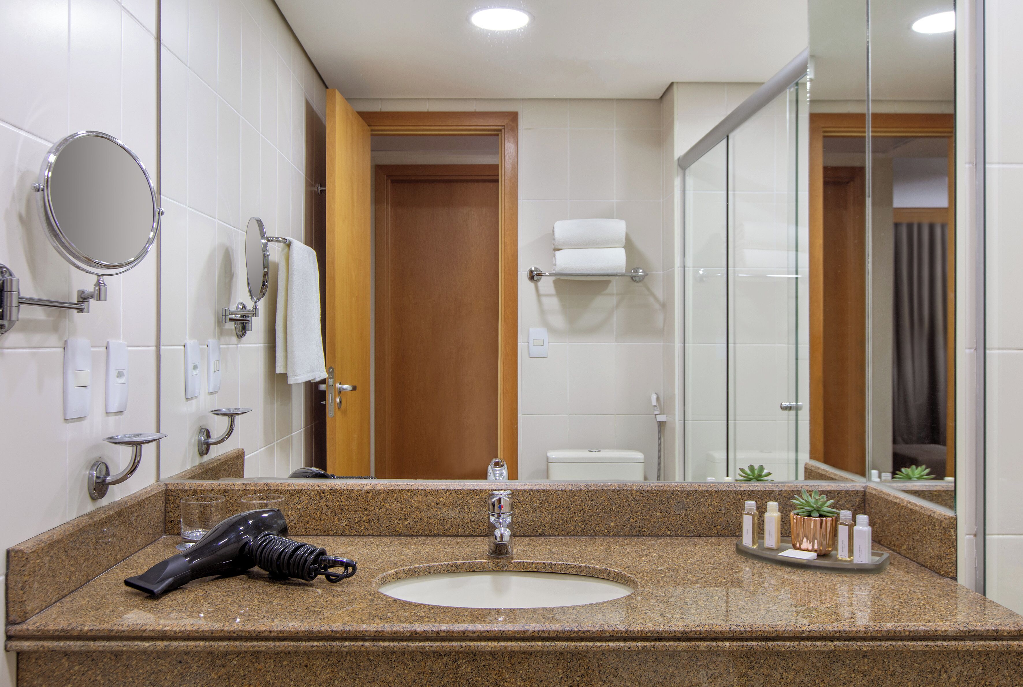 A hotel bathroom with a granite countertop, a sink, a mirror, a towel rack, and a glass shower enclosure.