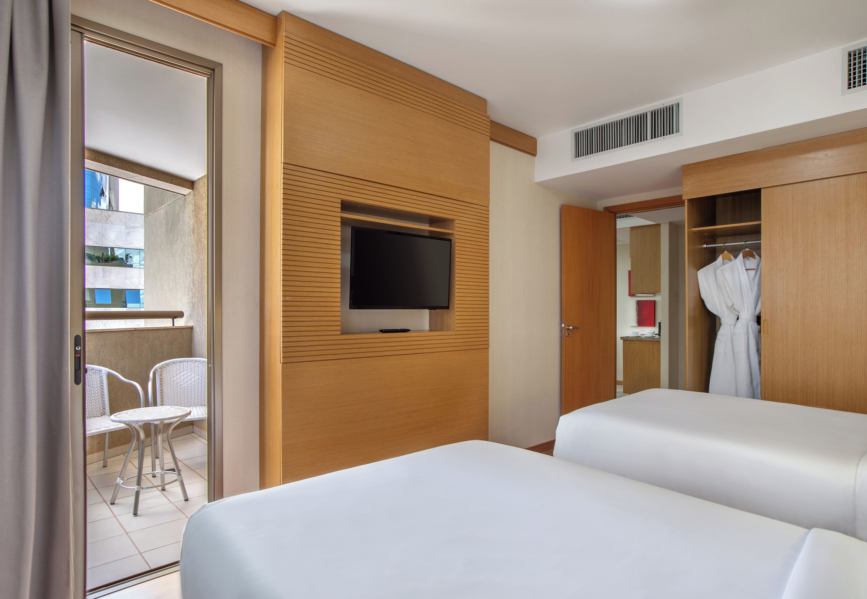 A hotel room with a balcony, a TV mounted on the wall, a wardrobe, and a bed.