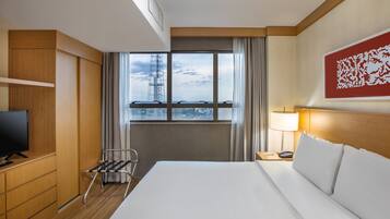 Une chambre d’hôtel avec un lit, une télévision, un bureau avec une lampe, une fenêtre avec des rideaux et une œuvre d’art rouge accrochée au mur.