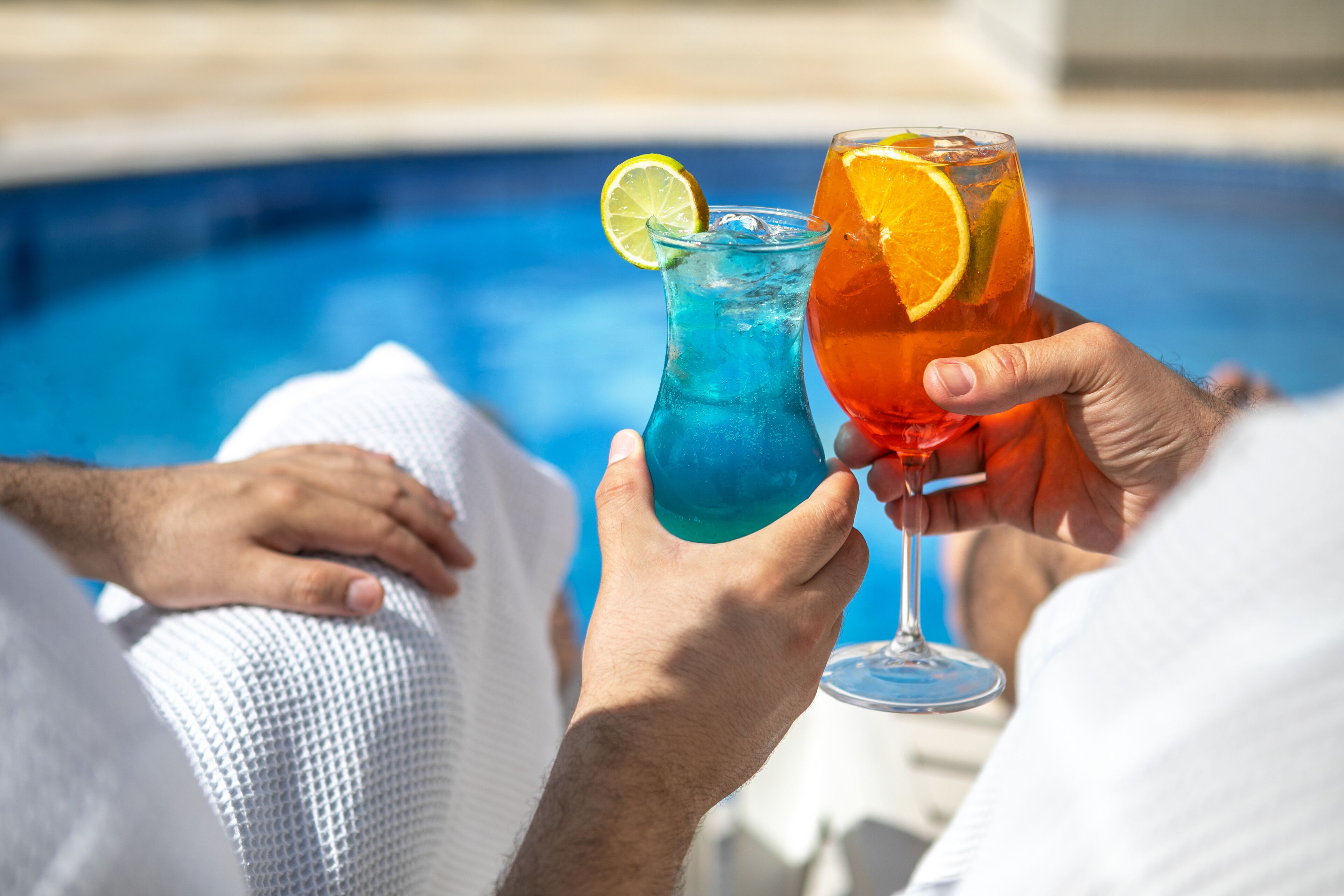 Deux personnes, chacune tenant un verre, sont assises au bord d’une piscine.