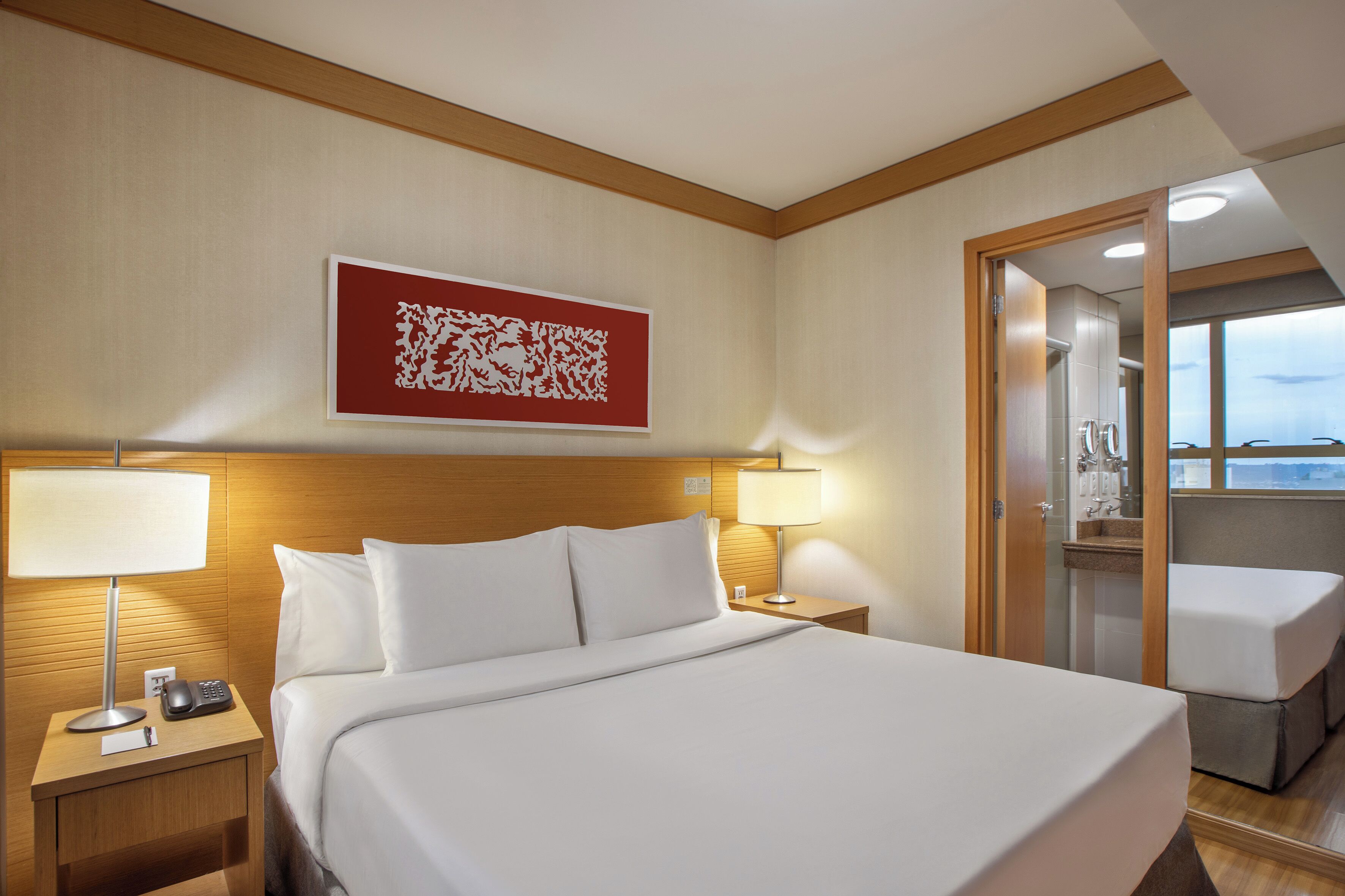 Habitación de hotel con una cama grande, una mesita de noche con lámpara, teléfono y una obra de arte colgada en la pared.